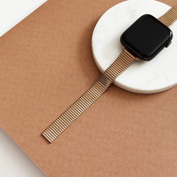 Rose gold slim Apple Watch strap with fine lines displayed on white marble, brown background.