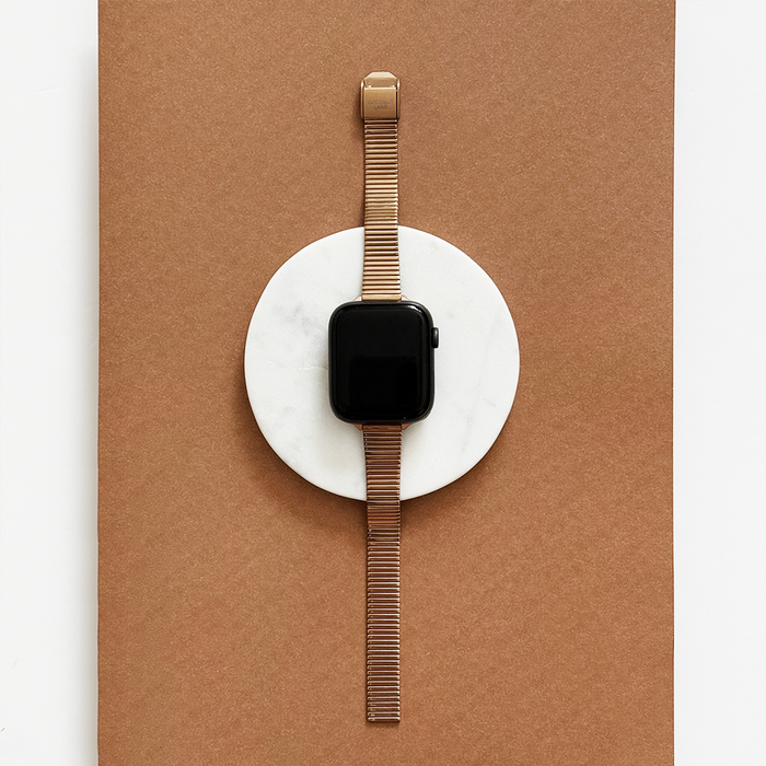 Rose gold SLIM Fine Line Apple Watch strap from Coconut Lane displayed on a white circle with a brown background.