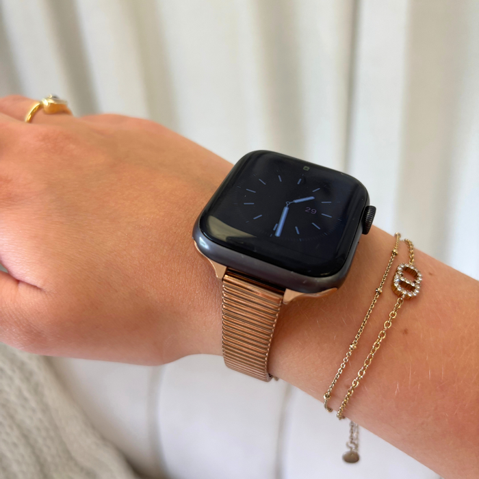 Gold Apple Watch with a slim rose gold metallic strap and two thin gold bracelets on the wrist.