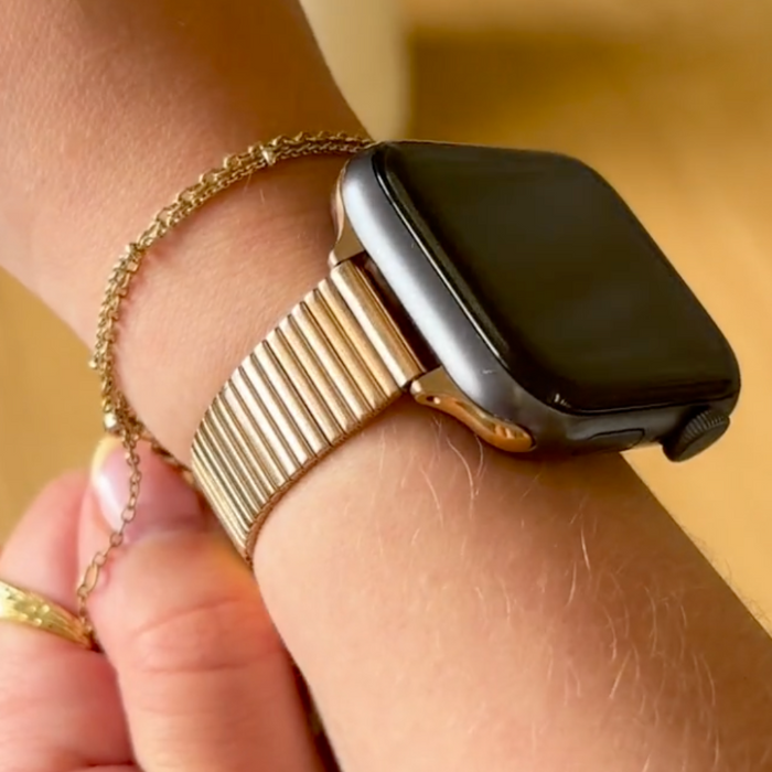 Wrist with a slim rose gold Apple Watch strap and a delicate chain bracelet.