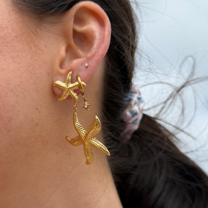Close-up of a woman wearing gold starfish earrings and a small stud from Coconut Lane.