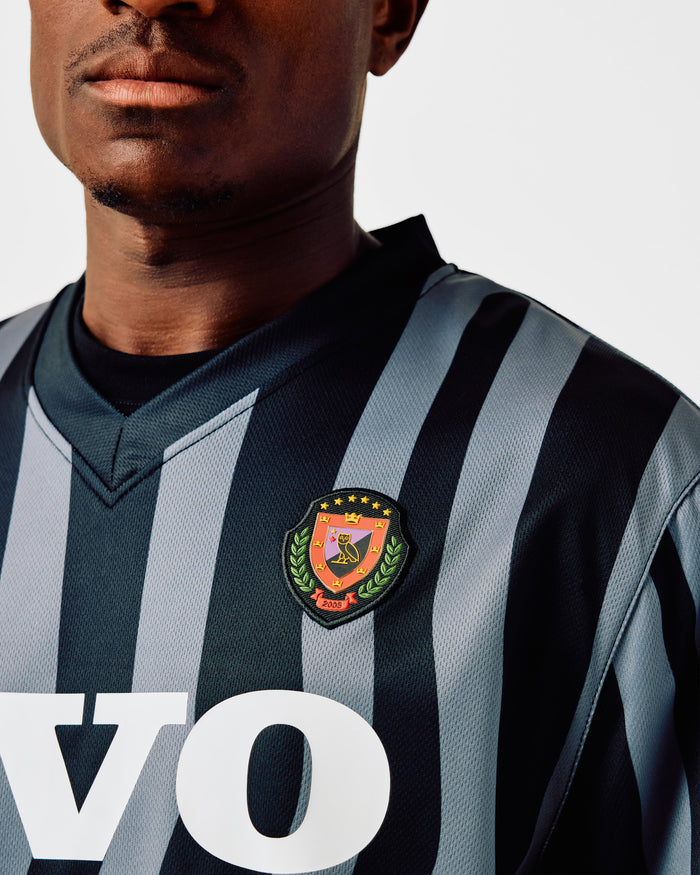 Black and gray striped soccer jersey with embroidered crest badge on chest.