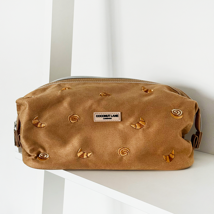 Gold-embroidered suedette expandable makeup bag in beige on a white shelf.