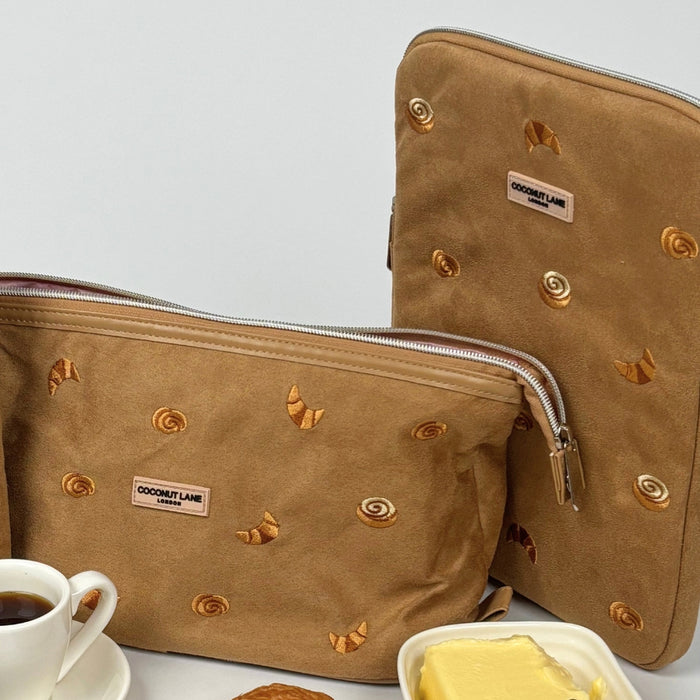 Two suedette iPad sleeves with croissant pattern by Coconut Lane, shown next to butter, a croissant, and coffee.