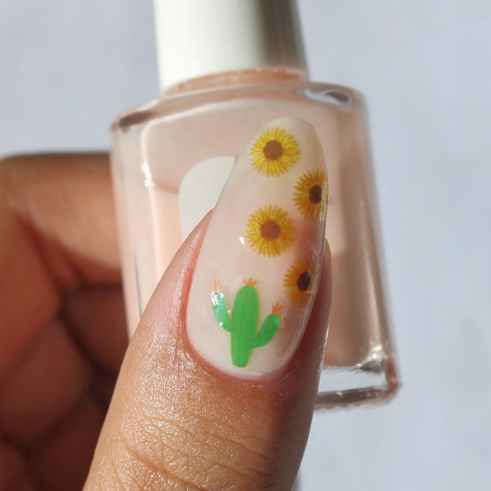 Take Me to the Desert sunflower and cactus decal on a sheer nude nail, holding the bottle
