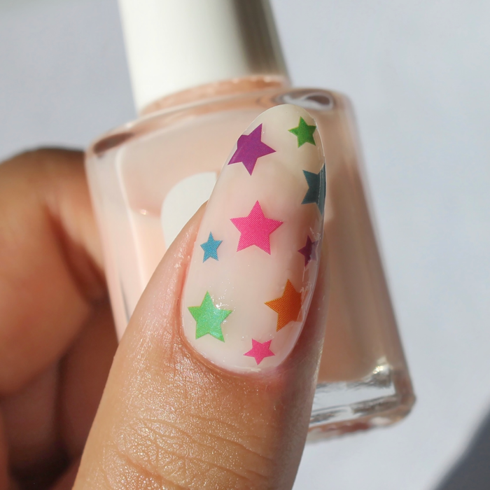 The Stars Are Aligned rainbow star decals on a sheer nude nail, holding the bottle