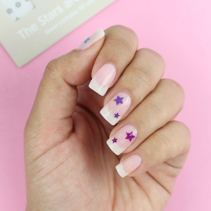 The Stars Are Aligned purple star decals on a sheer pink manicure with the packaging