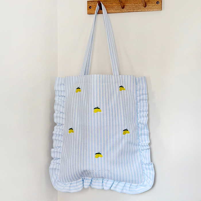Tote bag with ruffled edges and yellow lemon print, hanging on a wall hook.