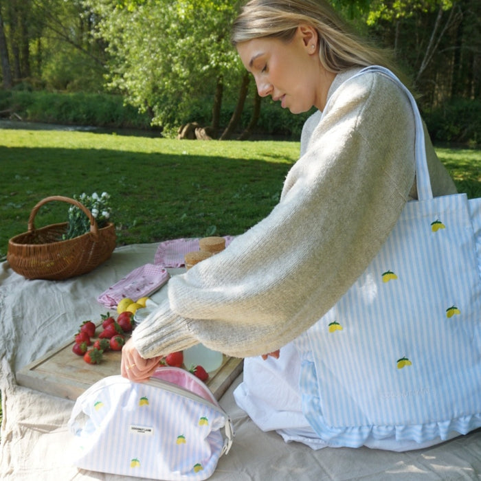 Woman at a picnic with a yellow lemon-print tote bag and matching pouch, reaching for berries.
