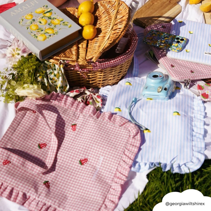Yellow lemon-patterned Coconut Lane tote bag on a picnic blanket with a book, flowers, and blue instant camera.