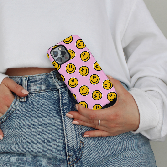 Person in jeans and a white sweatshirt holds a phone case with a yellow smiley face pattern.