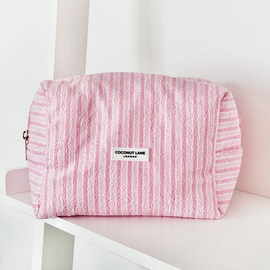 Powder Stripes towel makeup bag by Coconut Lane in pastel striped fabric displayed on a white shelf.