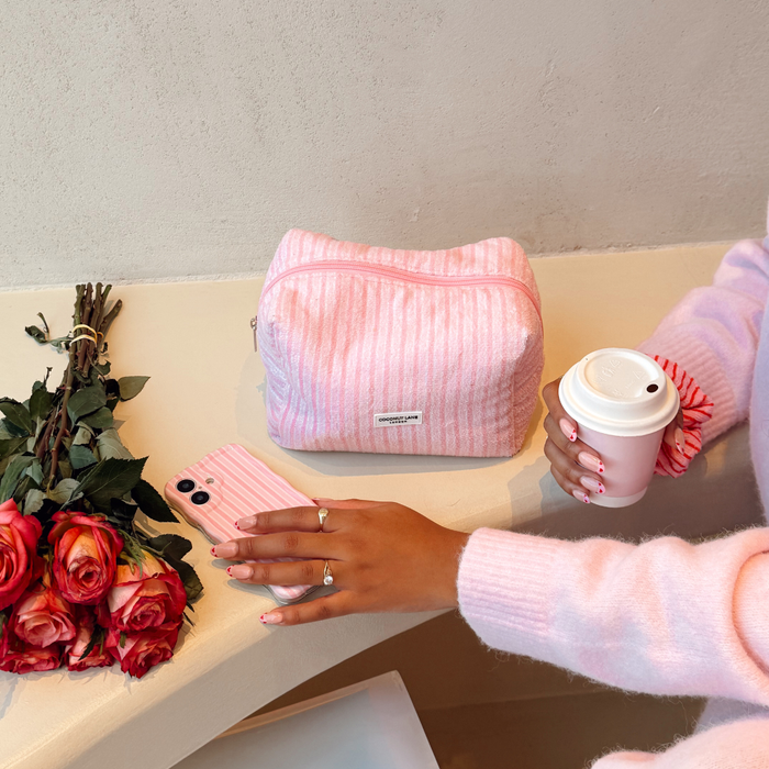Powder Stripes towel makeup bag and matching phone case from Coconut Lane next to roses, person in pink holding coffee.