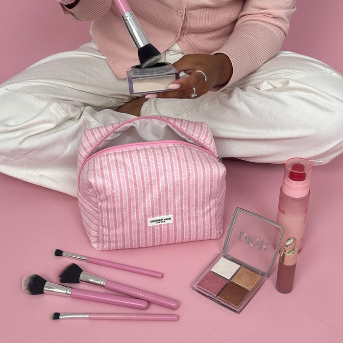 Coconut Lane Powder Stripes towel makeup bag with brushes, palette, lipstick, and spray next to person in pink and white.