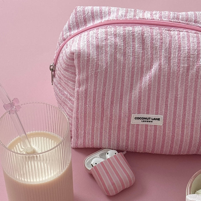 Coconut Lane AirPods Case with powder stripes pattern next to a glass of milk and straw on a pink background.