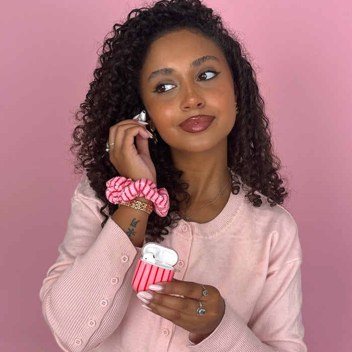 Woman with curly hair in a pink sweater wears a Coconut Lane Cherry Stripes towel scrunchie against a pink background.