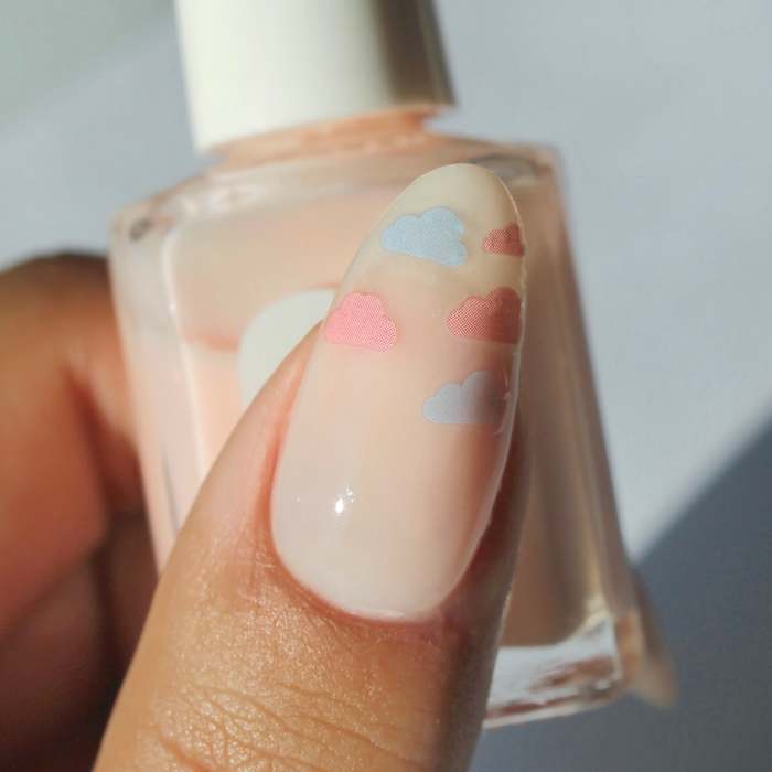 Up in the Clouds pastel cloud decals on a sheer nude nail, holding the bottle