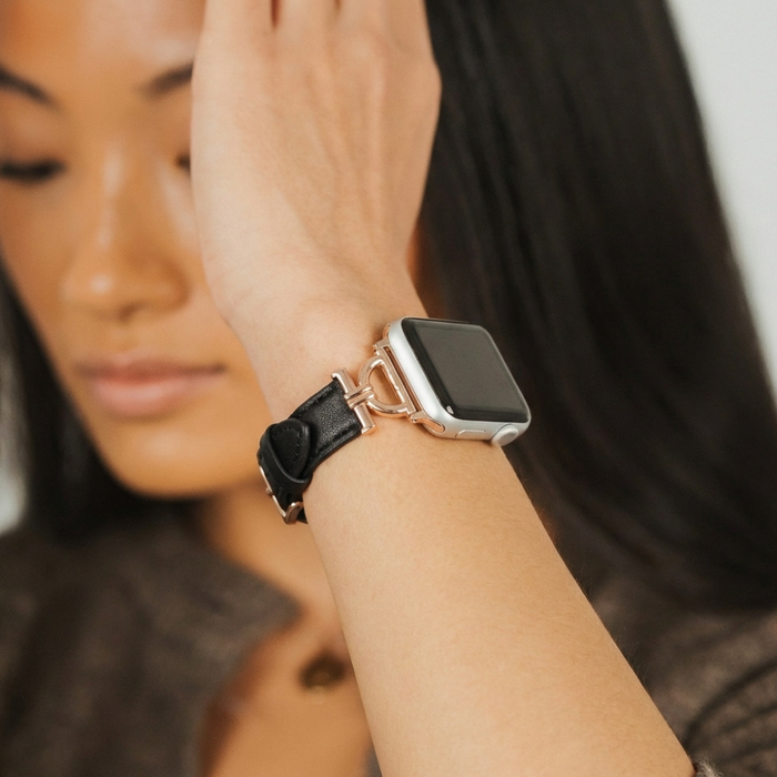 Woman with long hair wearing a black vegan PU leather Apple Watch strap, hand raised near her face.