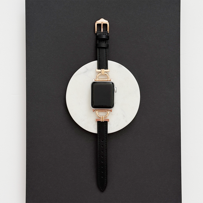 Kohl black vegan PU leather Apple Watch strap with gold hardware on a white marble surface.