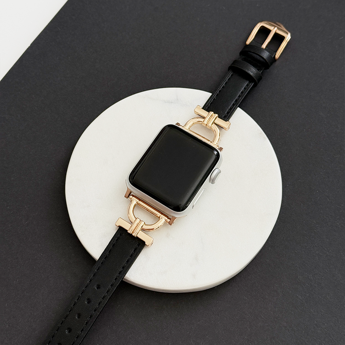 Kohl black vegan PU leather Apple Watch strap with gold-tone horsebit, displayed on a white marble surface.