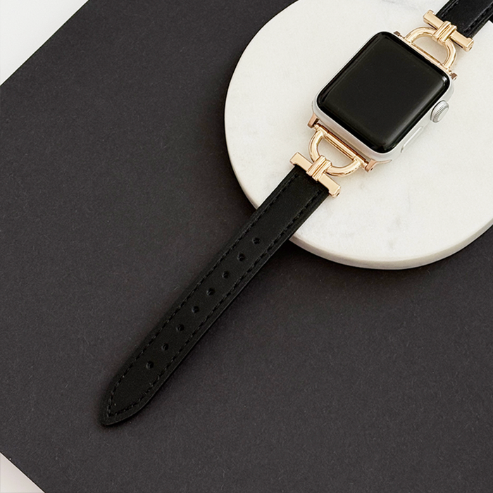 Black vegan PU leather Apple Watch strap with gold accents on a white oval dish.