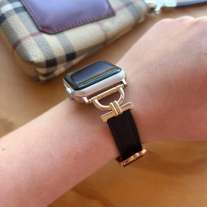 Black vegan leather Apple Watch strap on wrist next to a plaid wallet on a wooden surface.