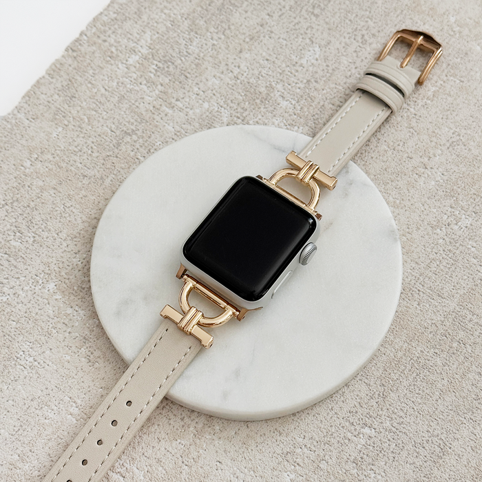 Oat-coloured vegan PU leather Apple Watch strap displayed on a round marble piece atop a textured beige background.