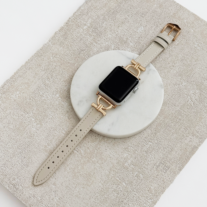 Gold Apple Watch with an oat-colored vegan leather strap on a white marble surface.