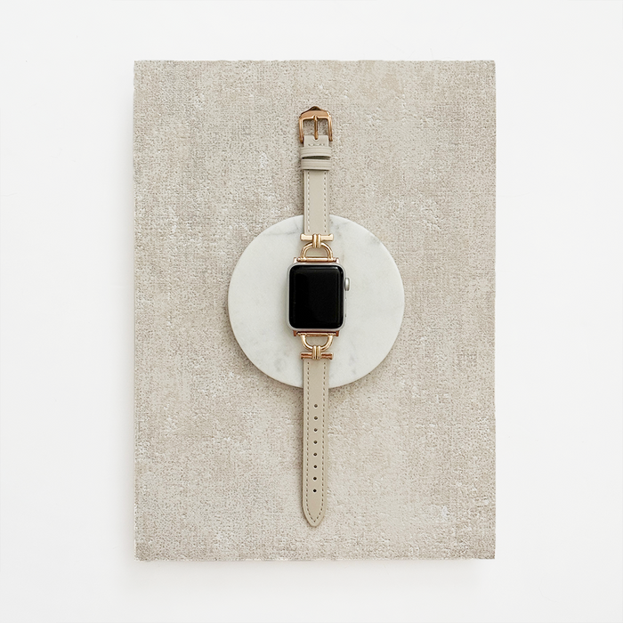 Oat-colored vegan PU leather Apple Watch strap displayed on a round marble slab against a textured beige background.