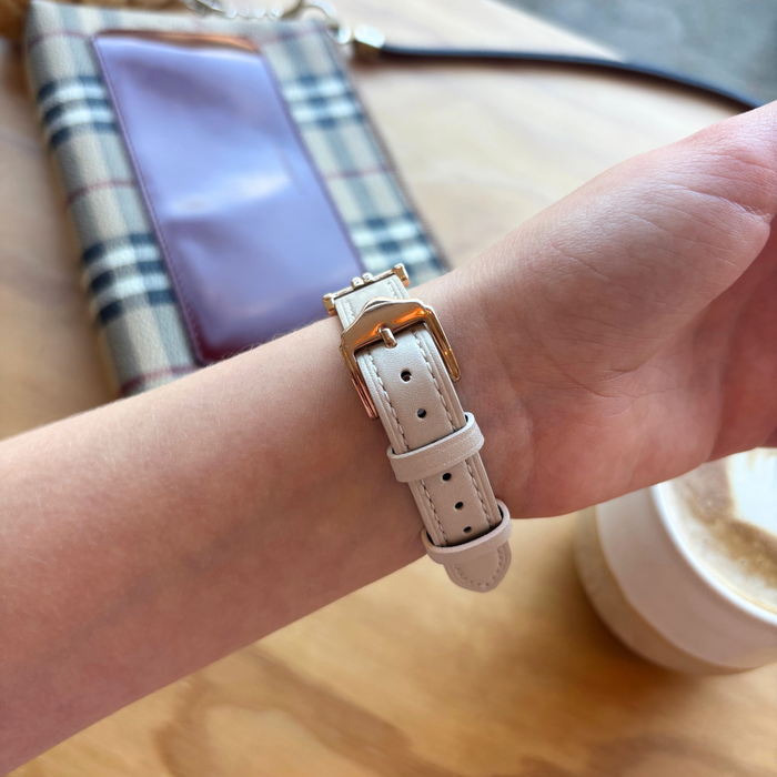 Hand wearing an oat-colored vegan PU leather Apple Watch strap, plaid purse and coffee cup in background.