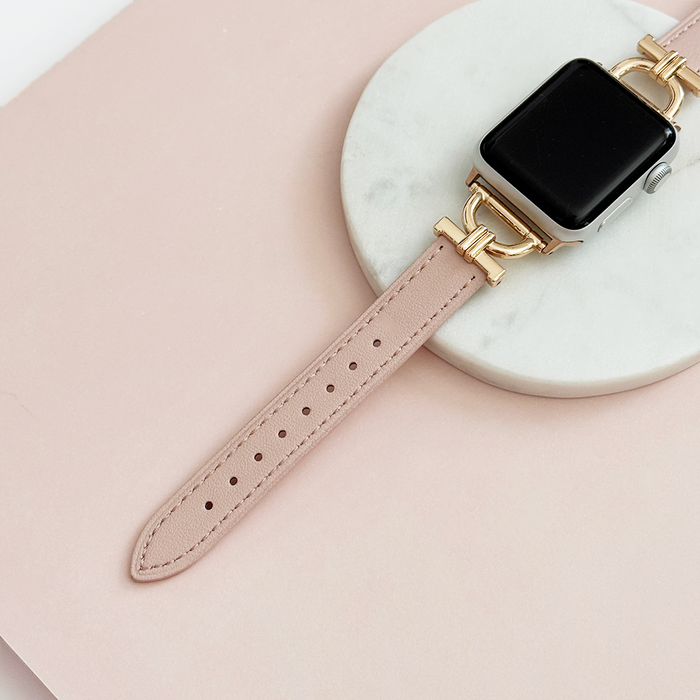 Gold smartwatch with a pink vegan leather strap on a marble tray.