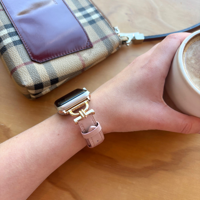 Pink vegan leather Apple Watch strap on wrist holding coffee next to a plaid purse on wooden surface.