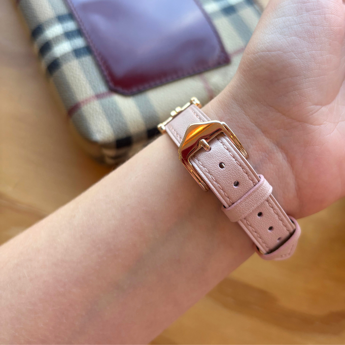 Wrist wearing pink vegan leather Apple Watch strap; plaid handbag blurred in the background.
