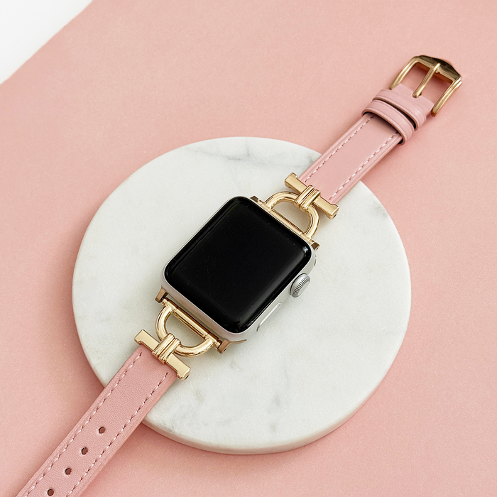 Powder pink vegan PU leather Apple Watch strap with gold hardware on a white marble tray.