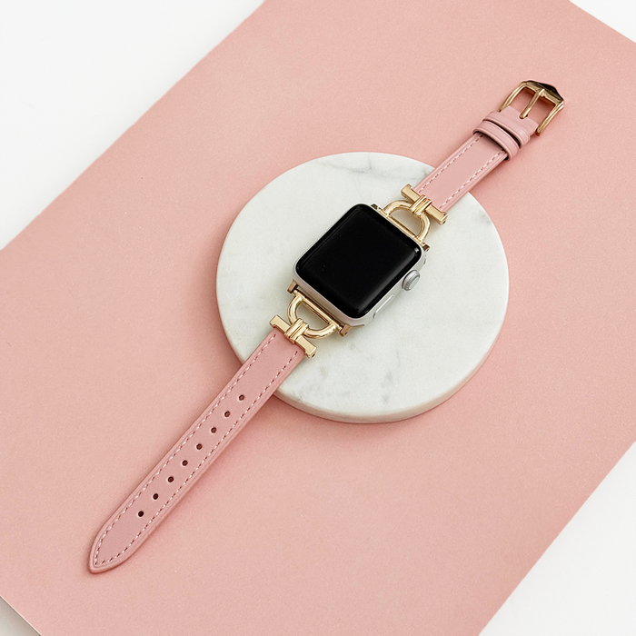 Powder pink vegan leather Apple Watch strap with gold links on white marble and a soft pink background.