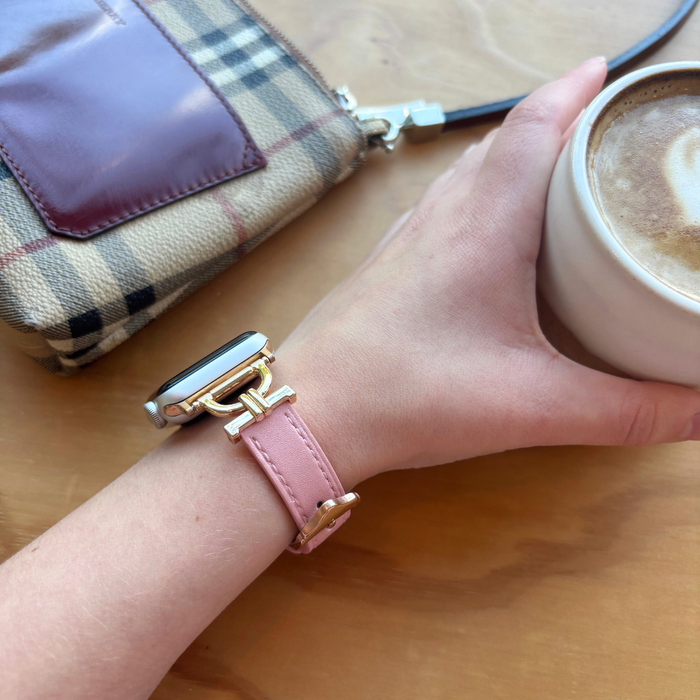 Powder pink vegan leather Apple Watch strap on wrist holding coffee next to a plaid wallet on wooden surface.