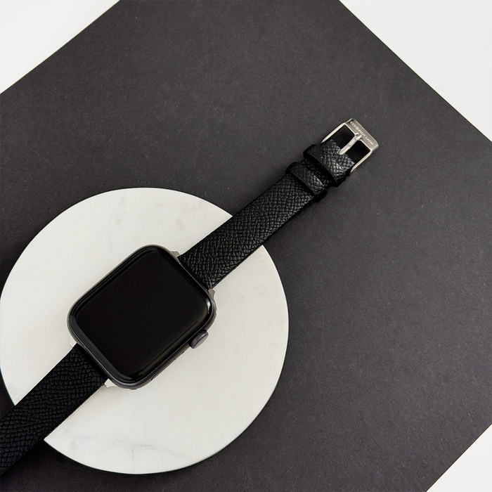Black textured vegan PU leather Apple Watch strap displayed on a white circle with a black square background.