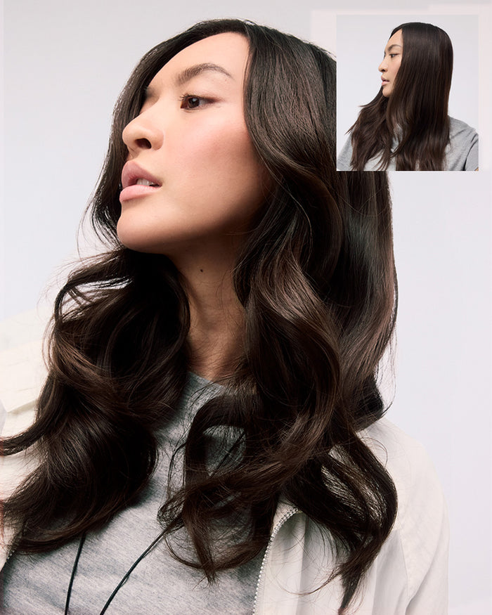 Woman with long, wavy hair wearing a gray sweater on a white background