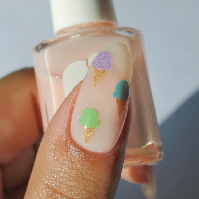 You Make Me Melt ice cream cone decals on a sheer nude nail, holding the bottle